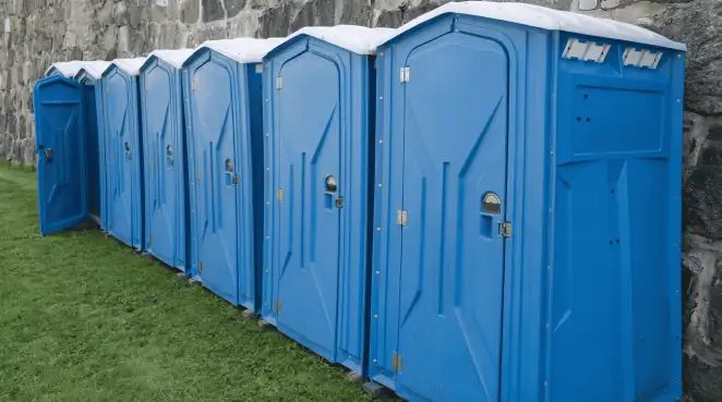 Row of blue portable toilets lined up on grass against a stone wall for event sanitation in Duluth, MN