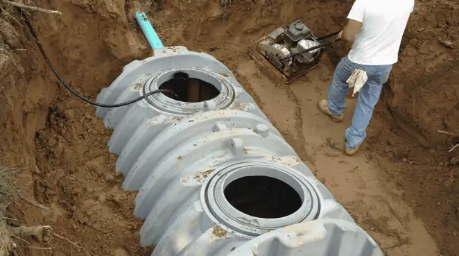 Septic tank installation showing a technician compacting soil around a new poly septic tank in an excavation pit in Duluth, MN